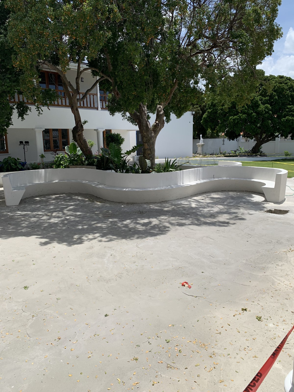 Finished white S-shaped concrete benches curve around mature trees at the EU head office, before the courtyard paving was complete