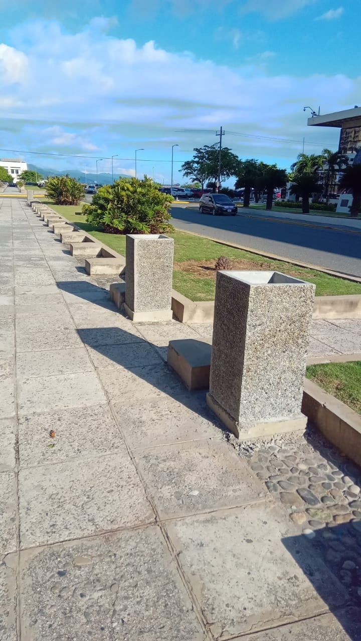 Tall square concrete planters with an exposed-aggregate finish, installed beside a paved promenade.