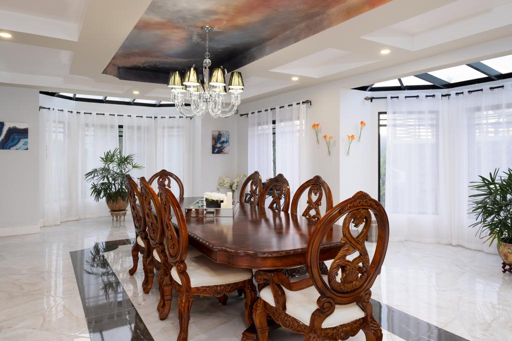 Breaking of the Dawn ceiling mural above Villa Mimosa’s carved wooden dining table and crystal chandelier, with the finished dining room furnished beneath it.